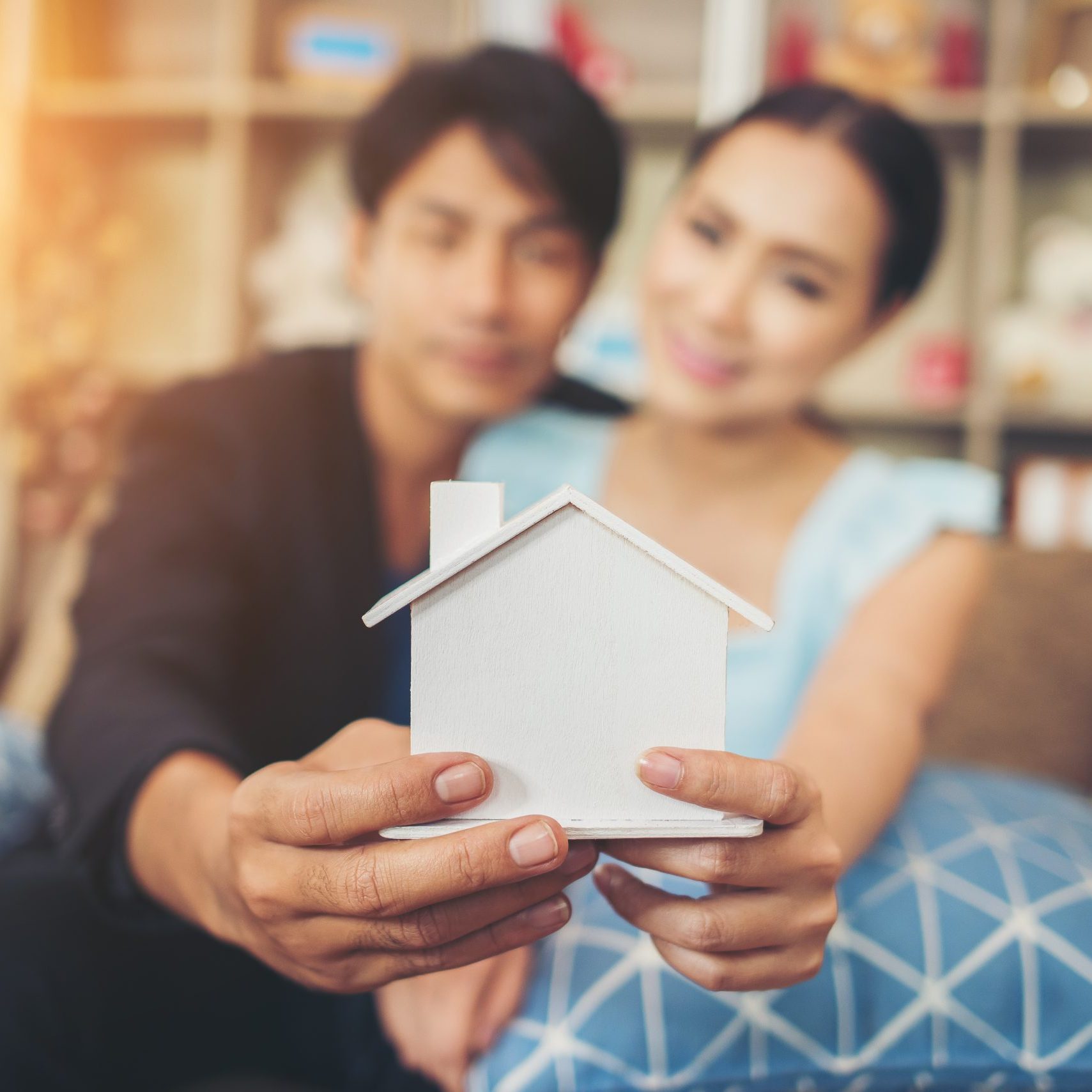 Young couple holding a white miniature house in living room